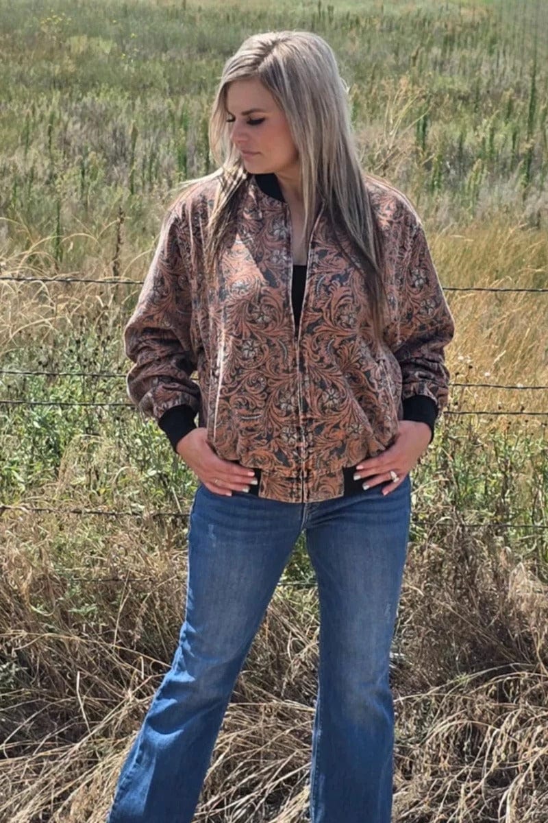 Woman wearing a browntooled  pattern jacket and blue jeans standing in a field.