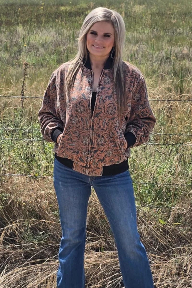 Woman wearing a tooled pattern jacket and blue jeans standing in a field.