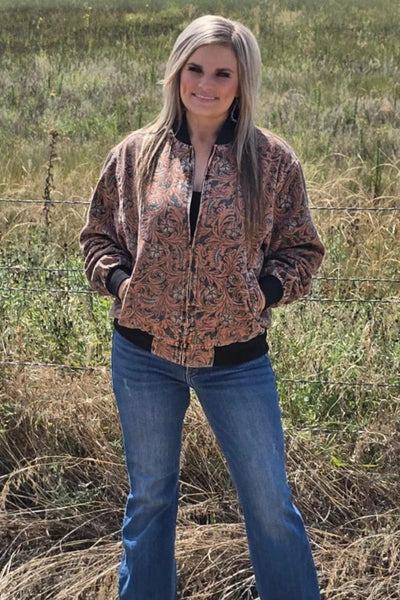 Woman wearing a tooled pattern jacket and blue jeans standing in a field.