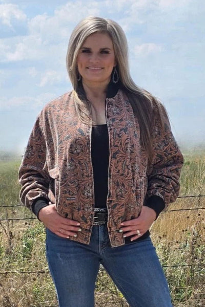 Woman wearing a tooled pattern jacket and blue jeans standing in a field with a clear sky.